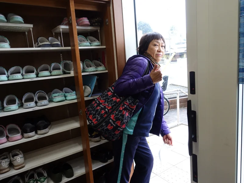 訪問に出かける玄関で、親指を立てて振り返る創業者・松田栄子