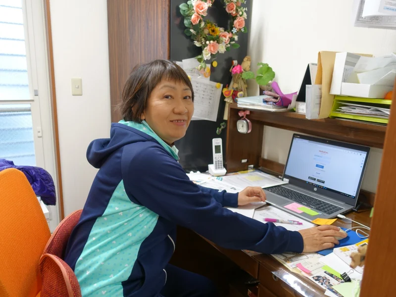 みよみよ看護の事務所で、パソコンに向かいながら笑顔で振り返る創業者・松田栄子