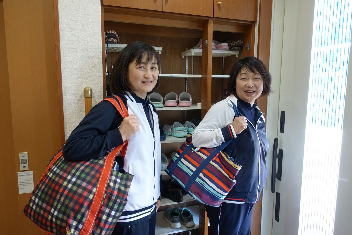訪問バッグを肩に笑顔で出発する看護師2名
